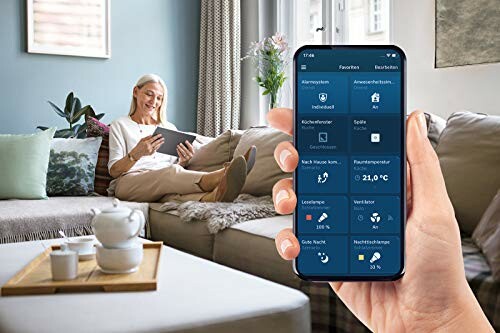 Frau nutzt Tablet im Wohnzimmer, während Smartphone Smart-Home-App zeigt.